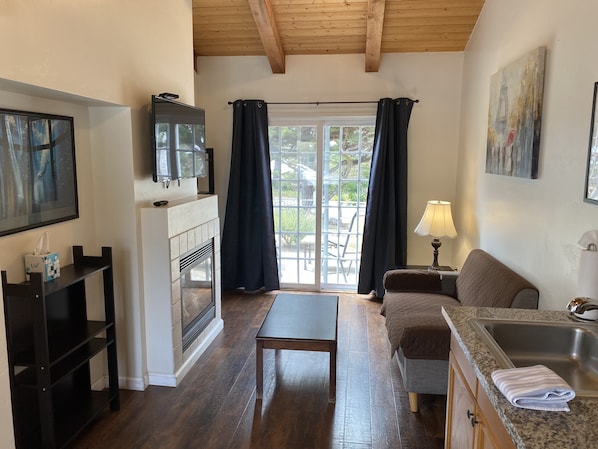 Una sala de estar acogedora con chimenea, televisor, sofá, mesa y una zona de cocina con fregadero y encimera.