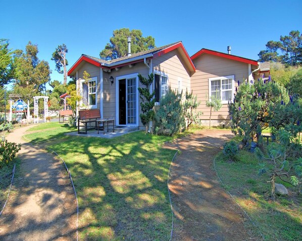 A two-story house with a red roof, a front porch, and a small garden.