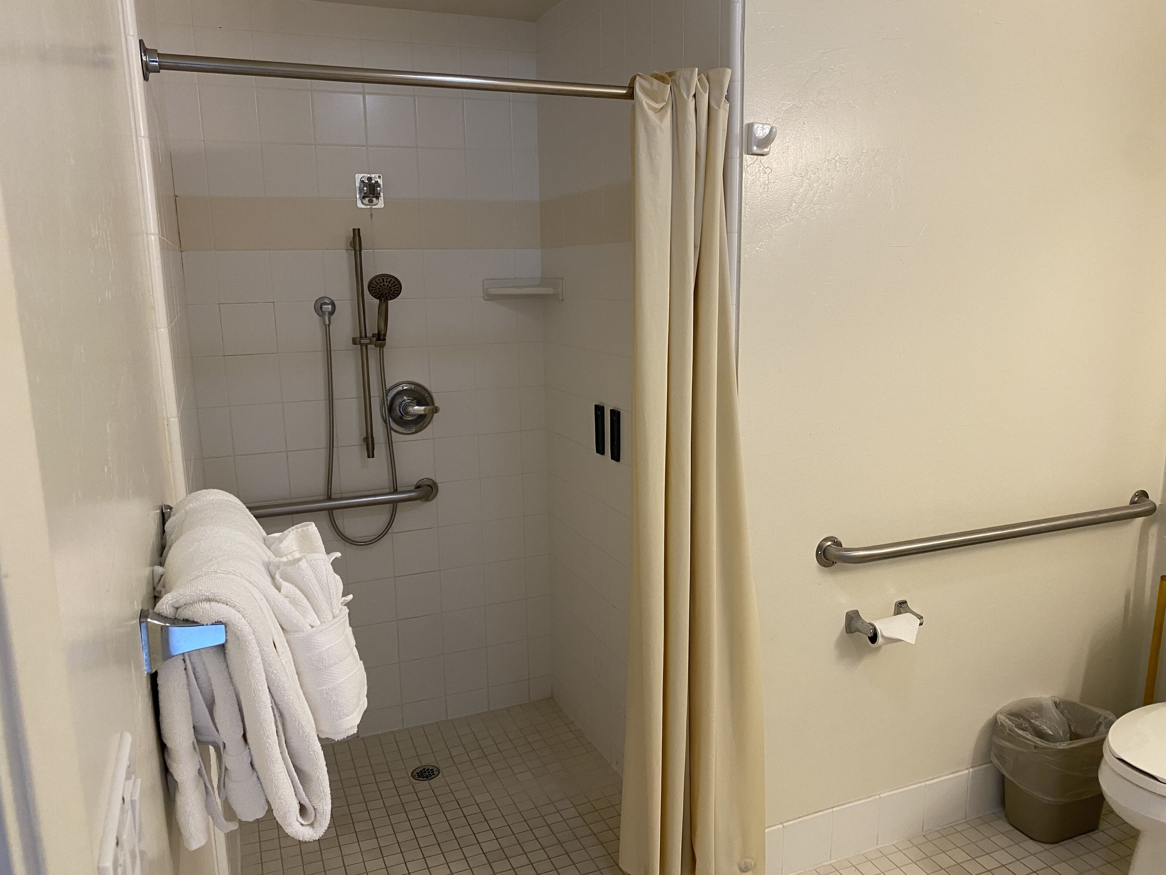 A shower area with a glass door, a towel rack with towels, a grab bar, and a trash can.