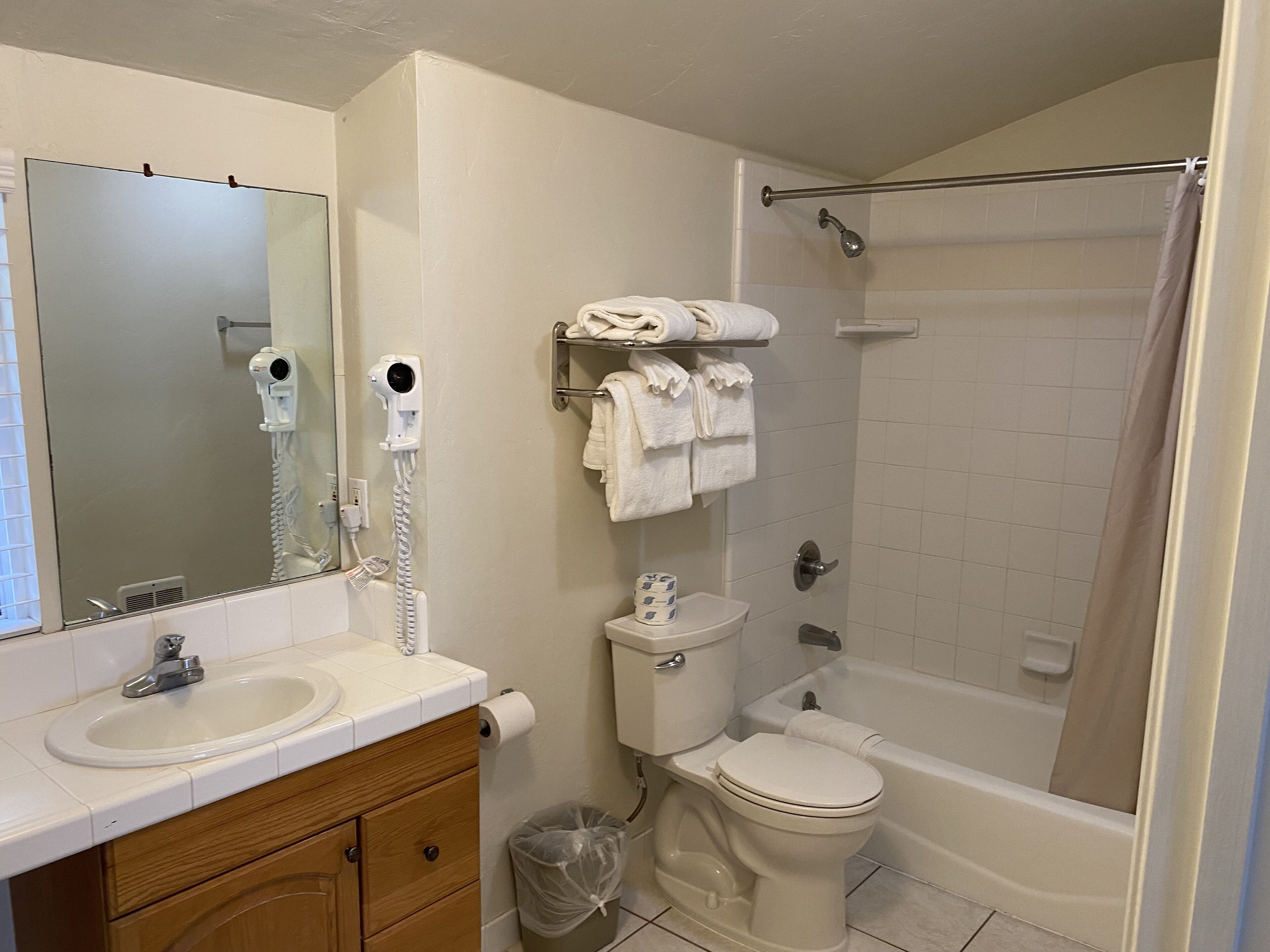 A bathroom with a sink, mirror, hair dryer, toilet, and bathtub.