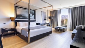 Una habitación de hotel moderna con una cama con dosel, un escritorio, un sofá y un amplio ventanal con cortinas.