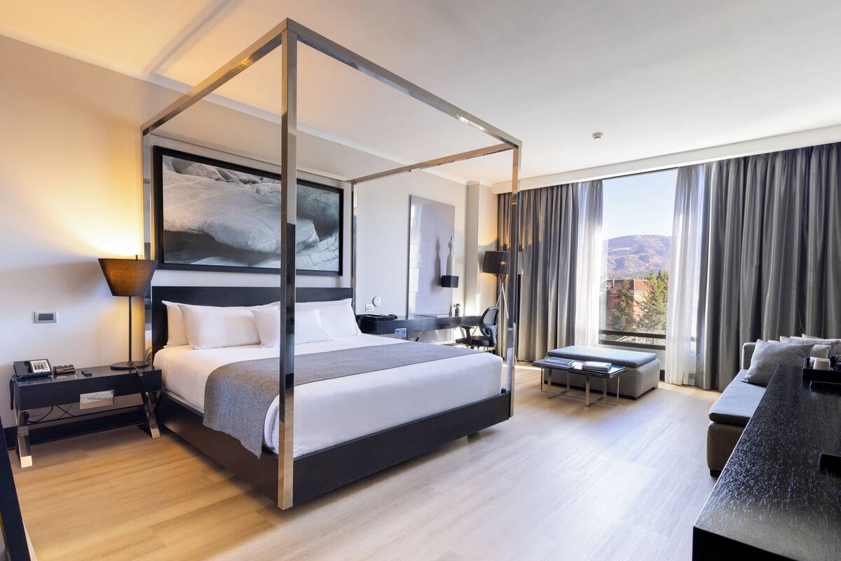 Een moderne hotelkamer met een hemelbed, een bureau, een bank en een groot raam met gordijnen.