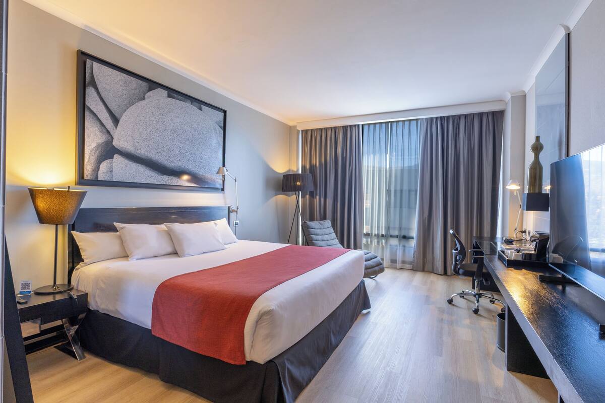 Een hotelkamer met een bed, bureau, stoel en een groot raam met gordijnen.