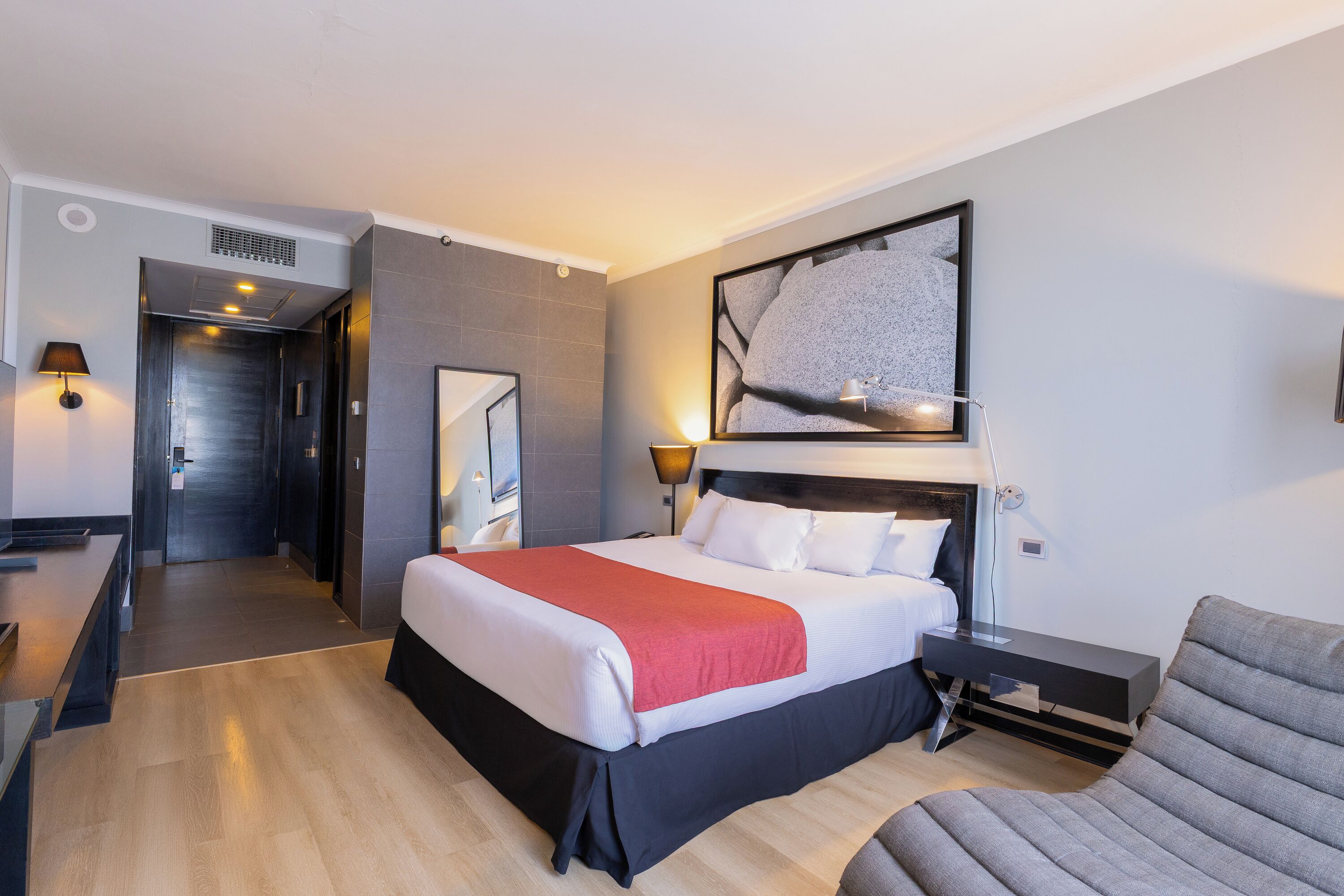 Une chambre d’hôtel avec un lit, des tables de chevet, une chaise, un bureau et une grande fenêtre.