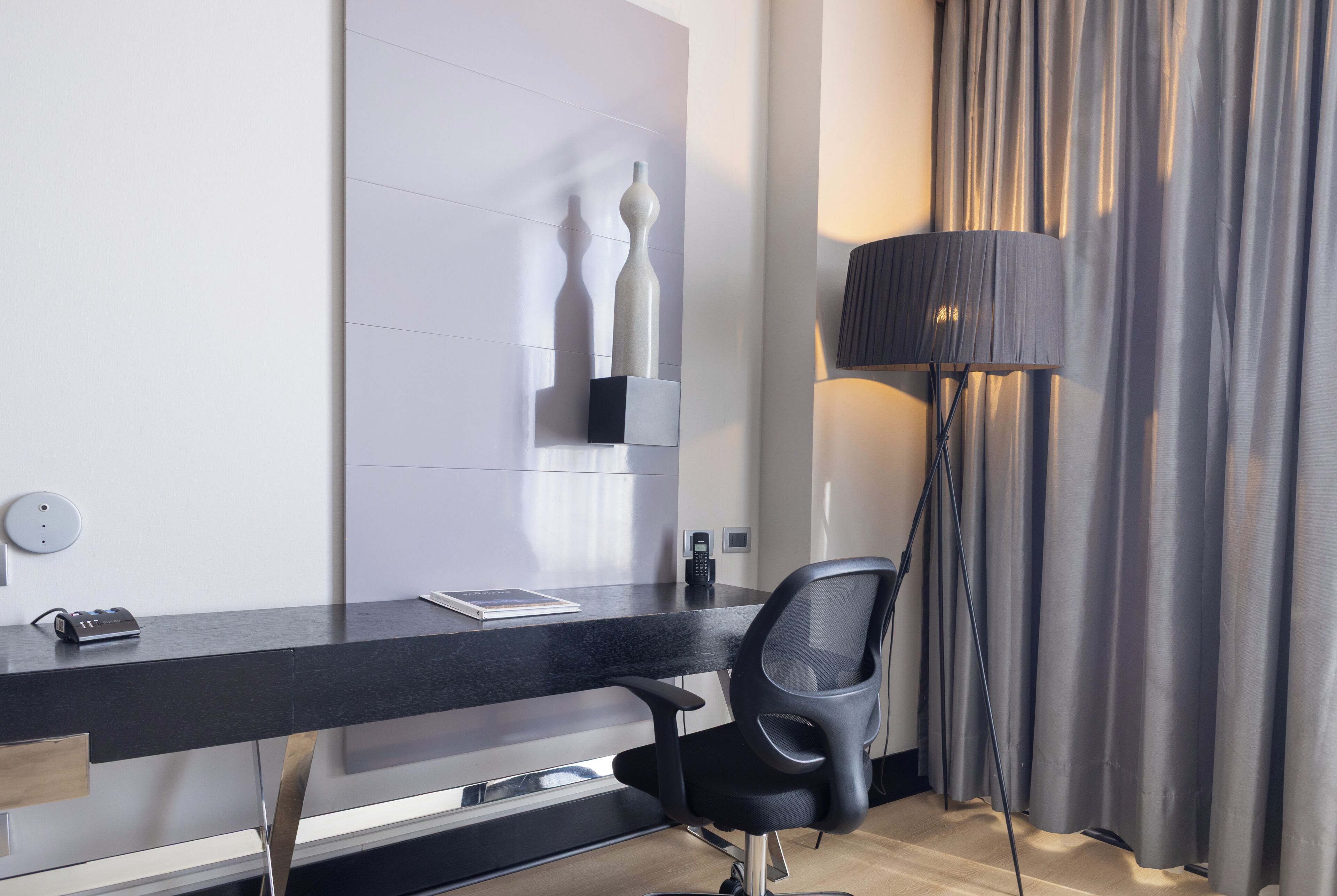 Ein modernes Hotelzimmer mit Schreibtisch, Stuhl, Lampe und Vorhängen.