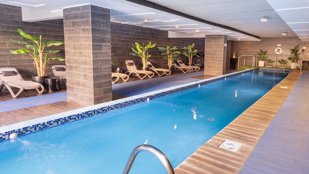 Una piscina interior con tumbonas, plantas en macetas y suelo de baldosas.
