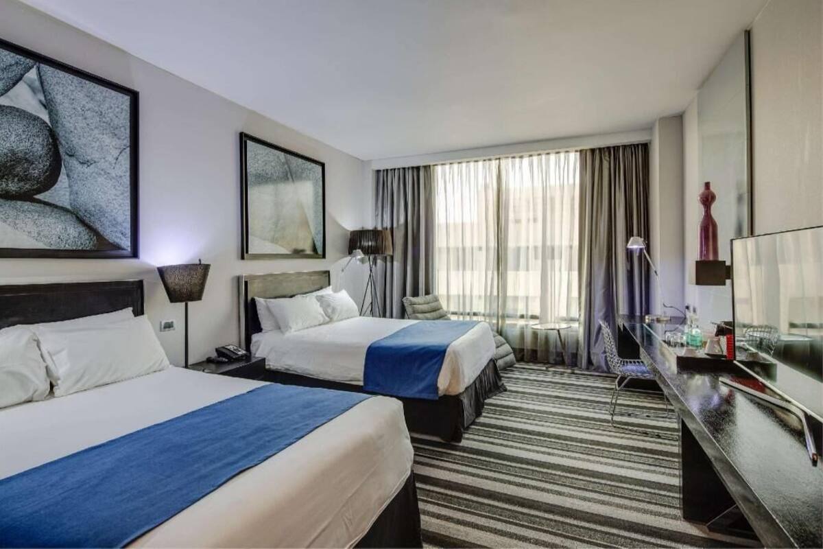 Hotelkamer met twee bedden, een bureau, een stoel, een televisie en een groot raam met gordijnen.