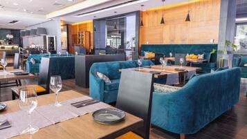 A modern restaurant with teal upholstered seating, wooden tables, and pendant lighting.