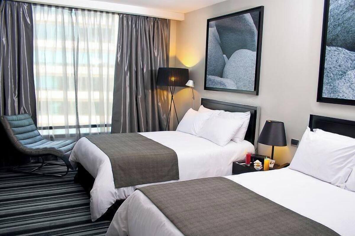 Een hotelkamer met twee bedden, een stoel, een lamp en kunst aan de muren.