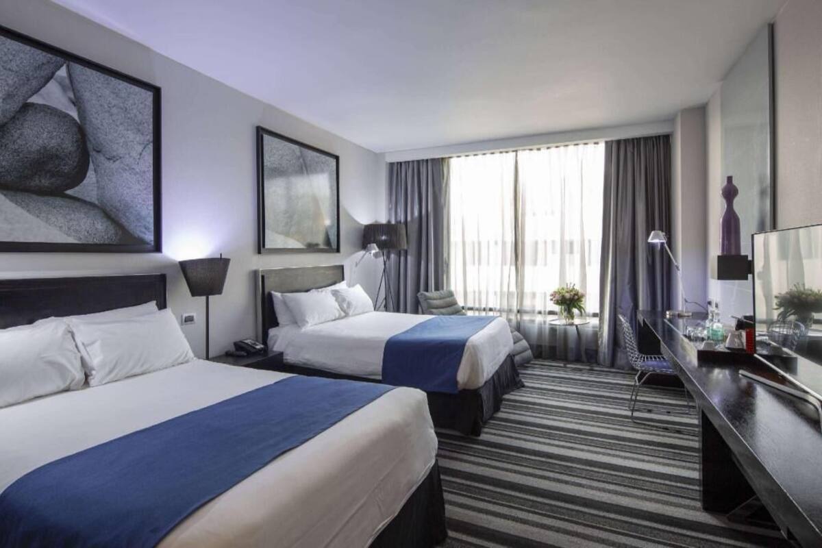 Een hotelkamer met twee bedden, een bureau, een televisie en een groot raam met gordijnen.
