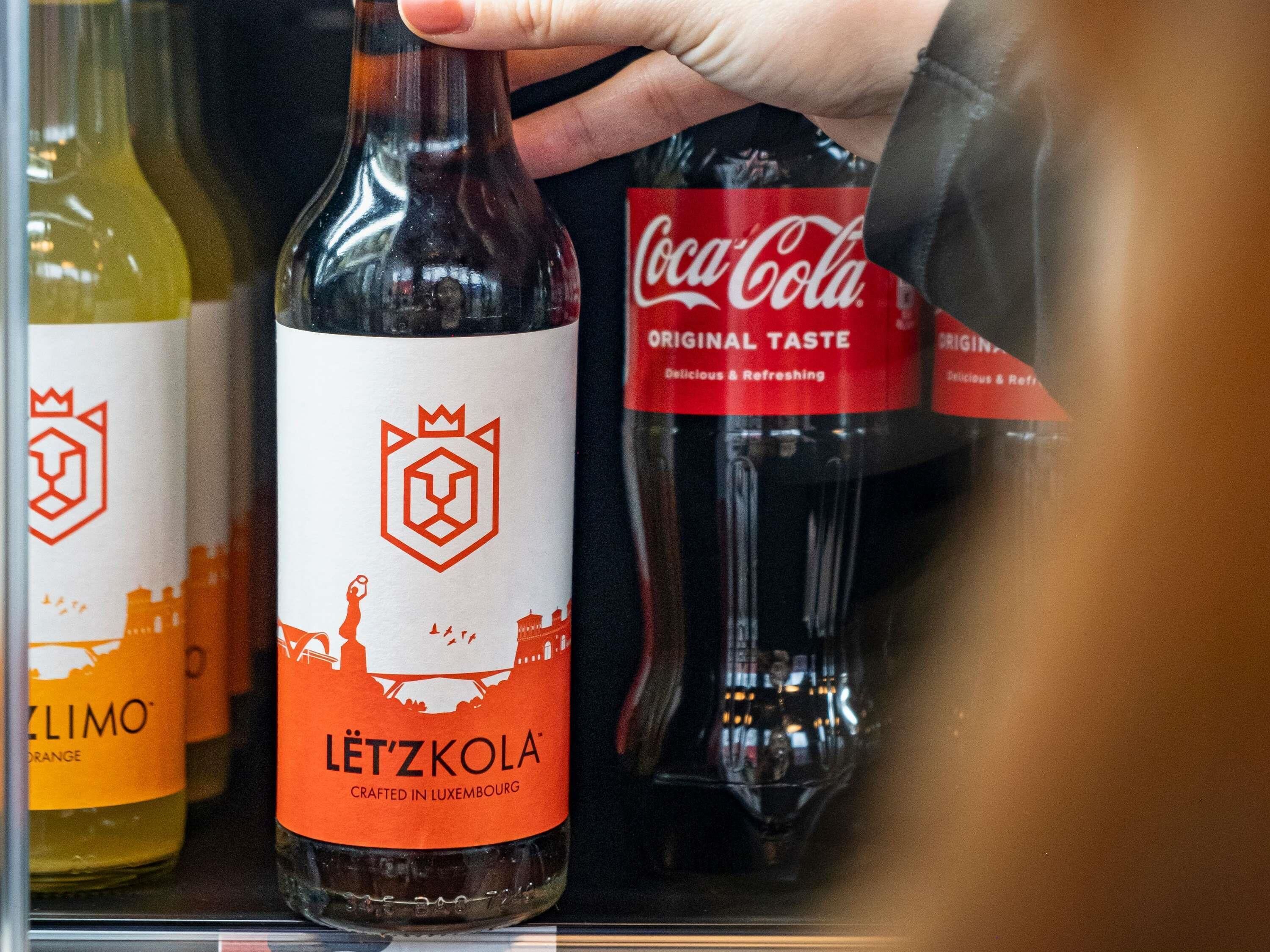A hand holding a bottle of Lützkola in a refrigerator.