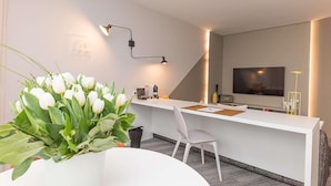 Un espacio de oficina moderno con un escritorio blanco, una silla, una planta en maceta, una máquina de café y un televisor montado en la pared.