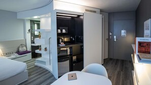 Una habitación de hotel moderna con kitchenette, una cama, una mesa con una botella y una silla.