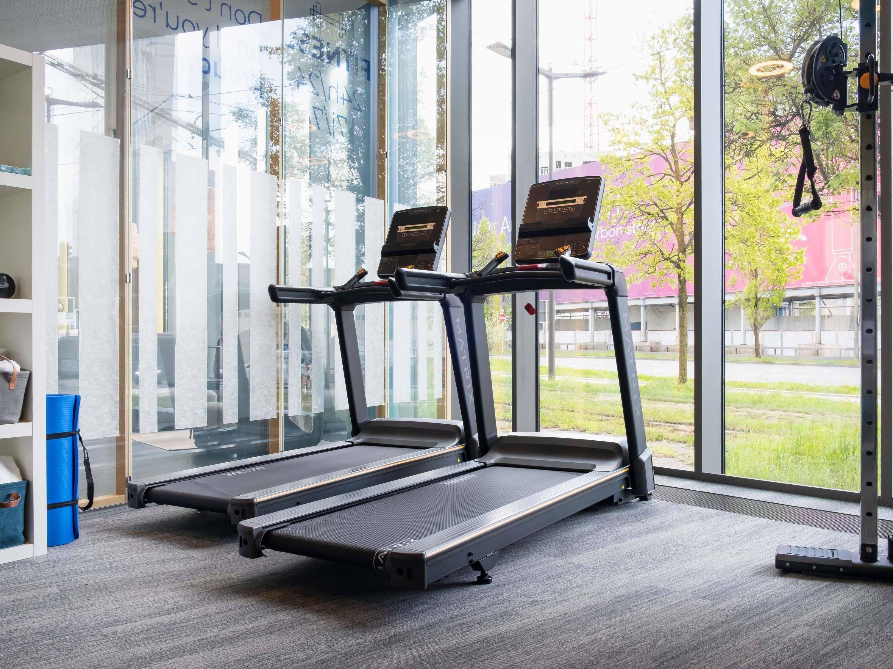 A gym with two treadmills, large windows, and a view of the outside.