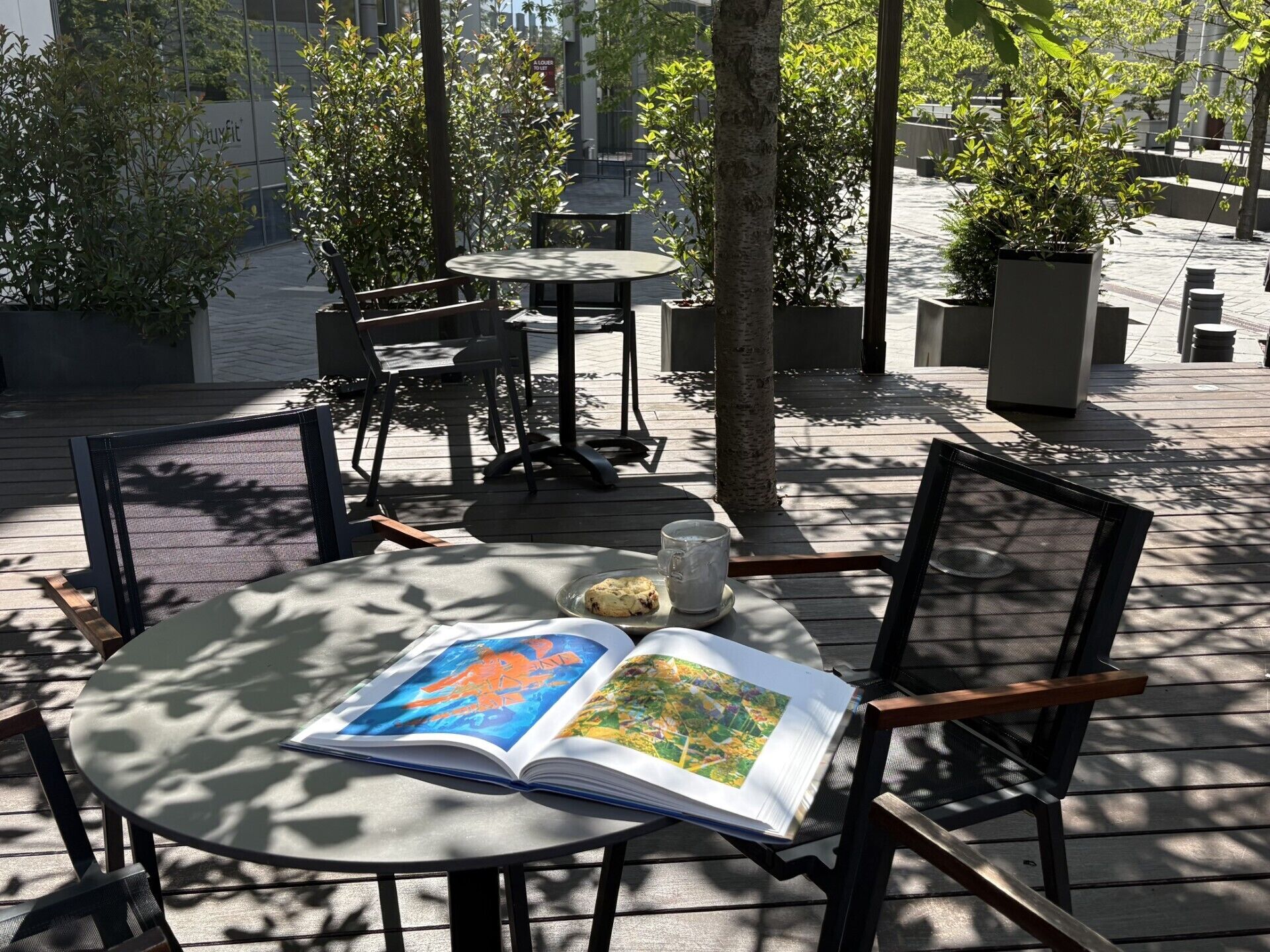 Un área exterior con mesas y sillas, un libro y un vaso de agua.