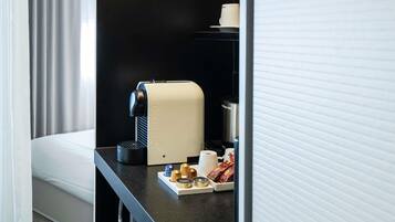 A hotel room with a black countertop, a Nespresso coffee machine, a cup of coffee, and a tray with coffee pods and a small container.