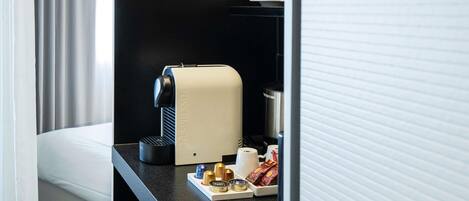 A hotel room with a black countertop, a Nespresso coffee machine, a cup of coffee, and a tray with coffee pods and a small container.