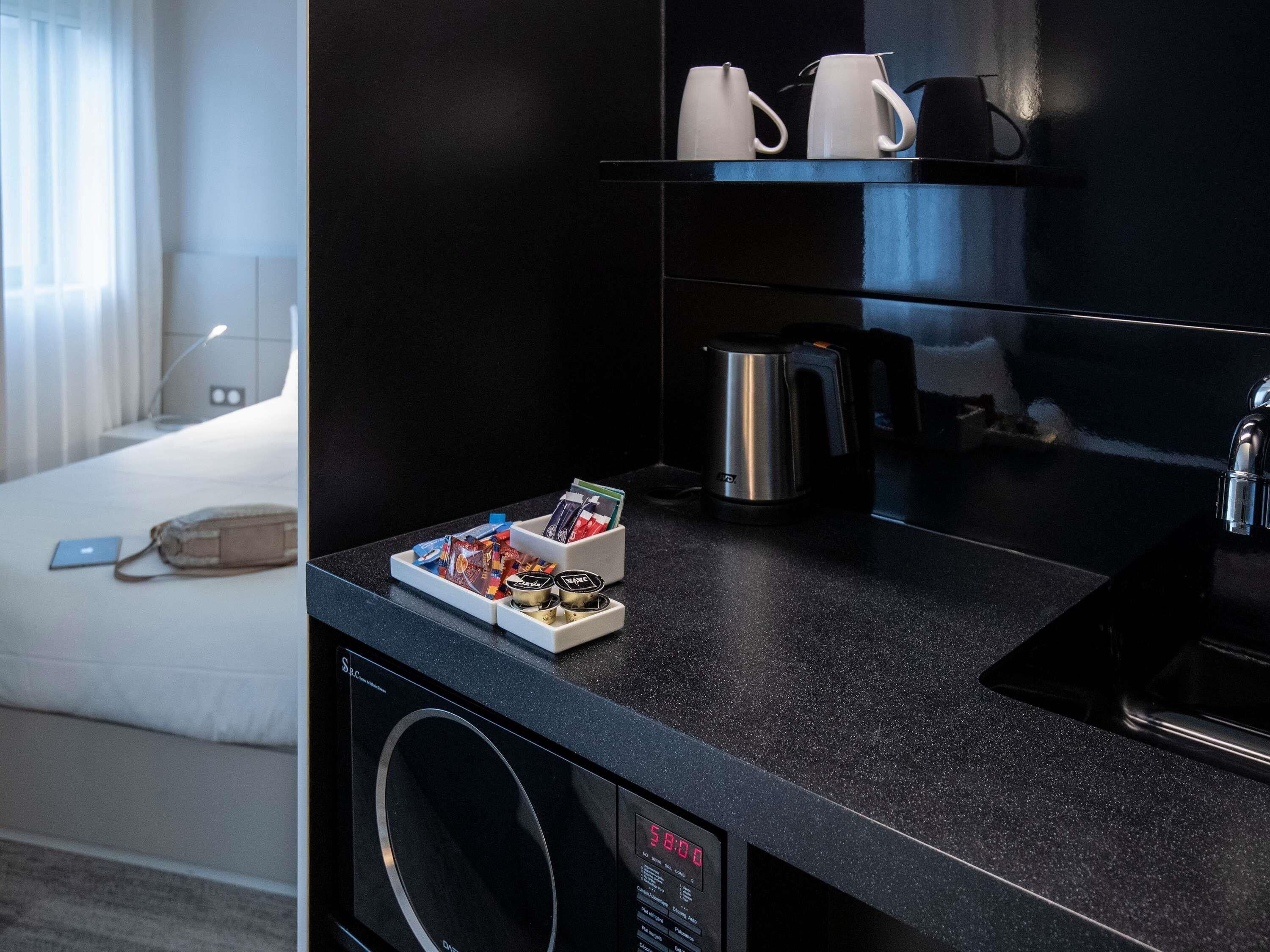 Een moderne hotelkamer met een zwart aanrecht, koffiezetapparaat, waterkoker en een kleine koelkast.