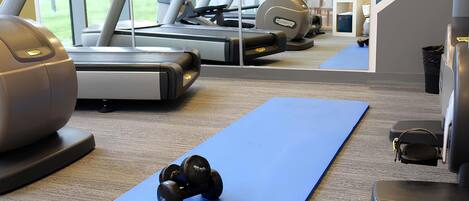 Un gimnasio con equipo de ejercicio, incluyendo cintas de correr, una máquina de remo y mancuernas sobre un tapete azul.