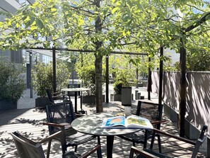 Un espace extérieur aménagé avec des tables et des chaises, entouré d’arbres et avec un bâtiment en arrière-plan.