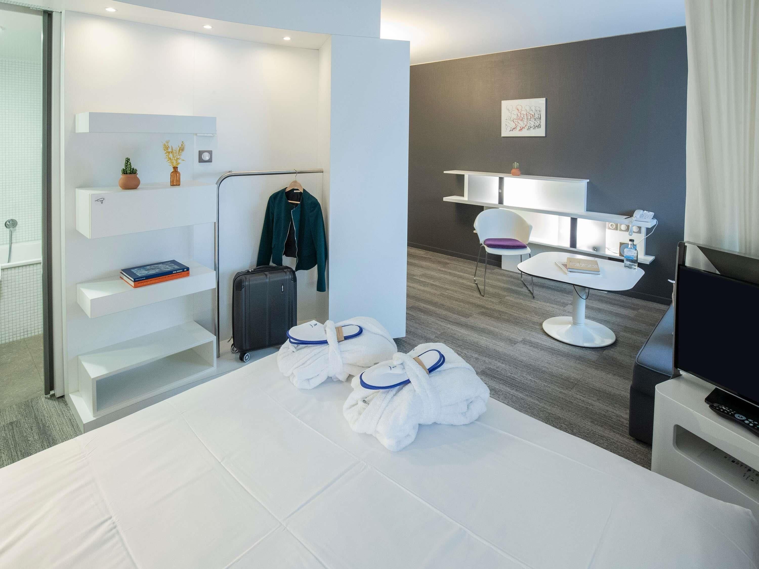 Una habitación de hotel moderna con cama, escritorio, silla, televisor y armario.