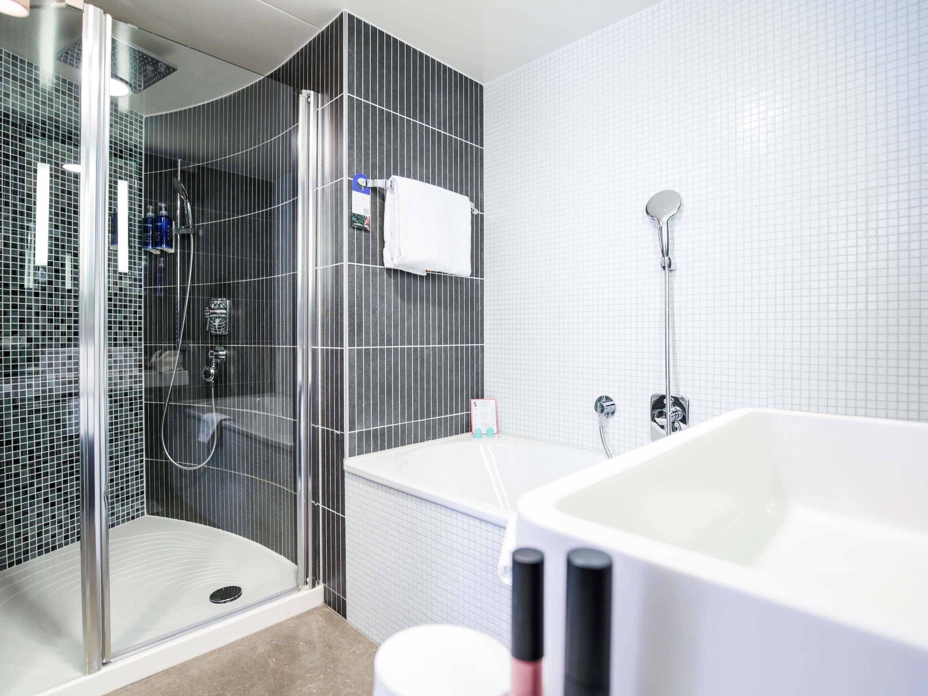 Un baño moderno con ducha envuelta en vidrio, una bañera blanca y un revestimiento de azulejos.