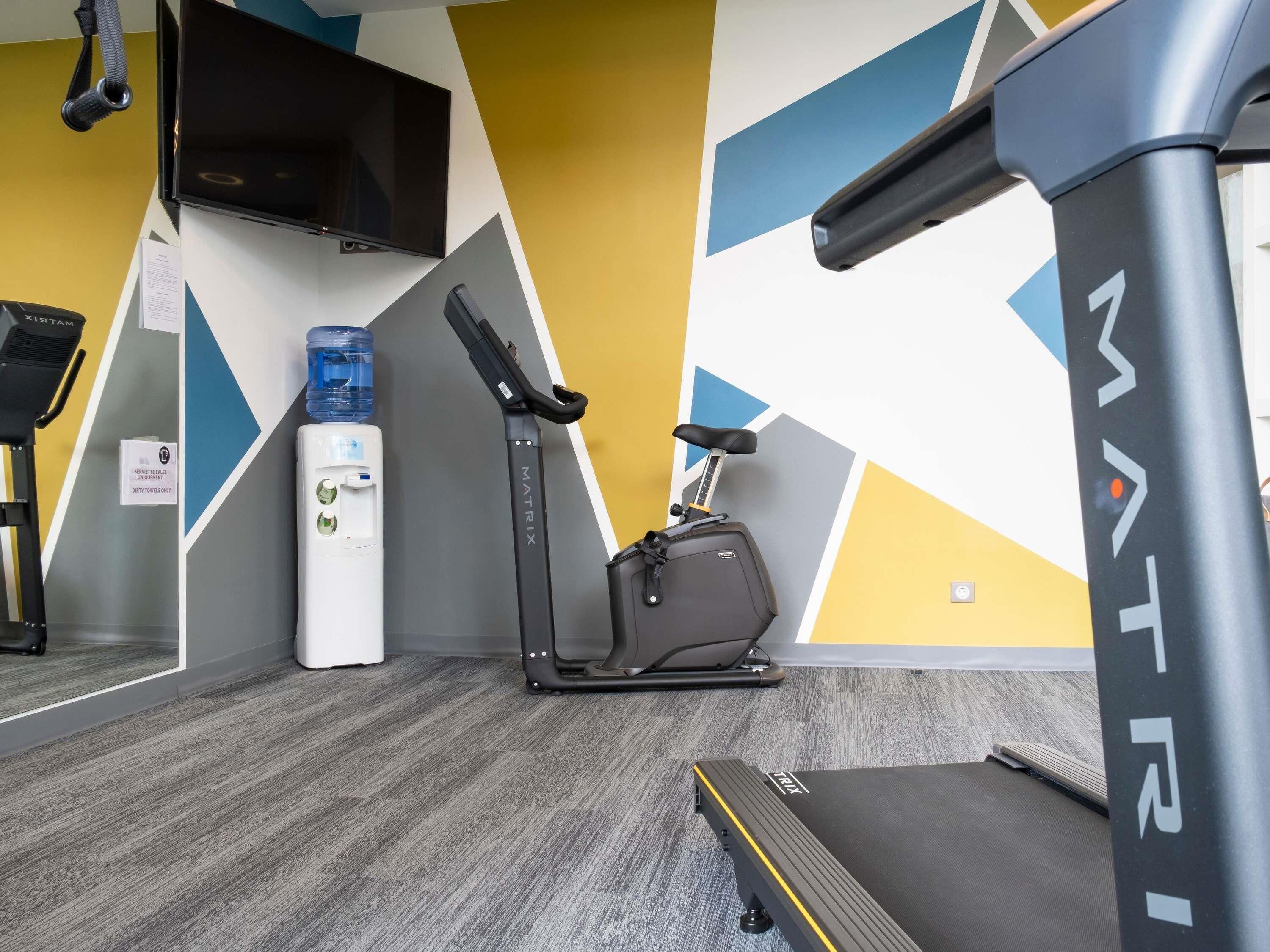 Ein Fitnessraum mit Laufband, Ergometer, Wasserspender und Trainingsgeräten.