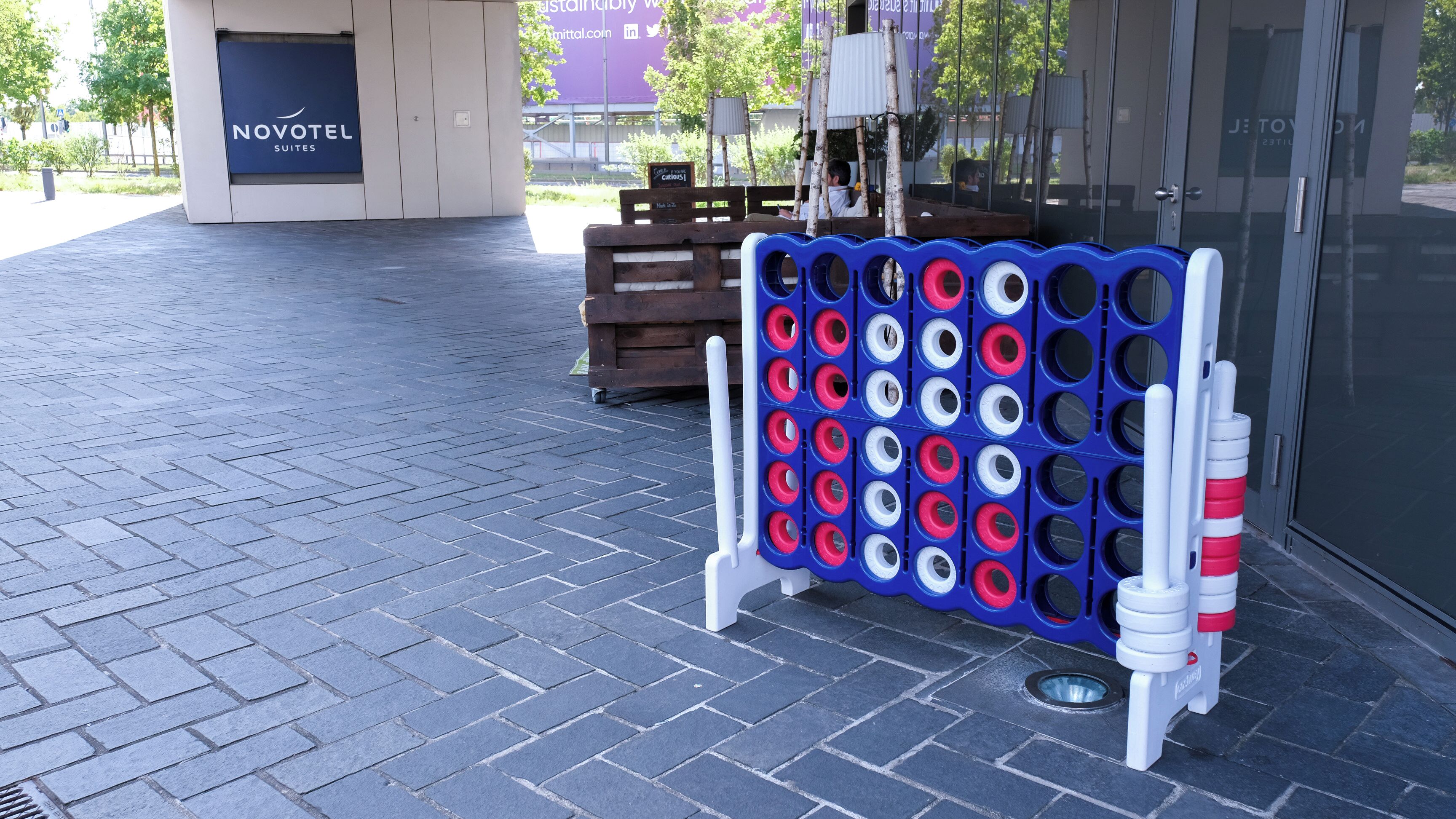 A blue and white game board with holes, a wooden bench, and a Novotel sign.