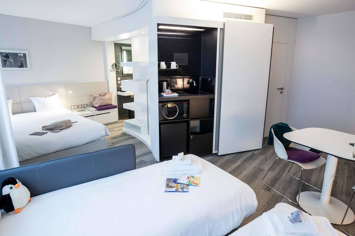 A hotel room with two beds, a kitchenette, a dining area, and a bathroom.
