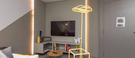 Una sala de estar moderna con un televisor de pantalla plana, una estantería, una mesita redonda y un sofá con cojines.