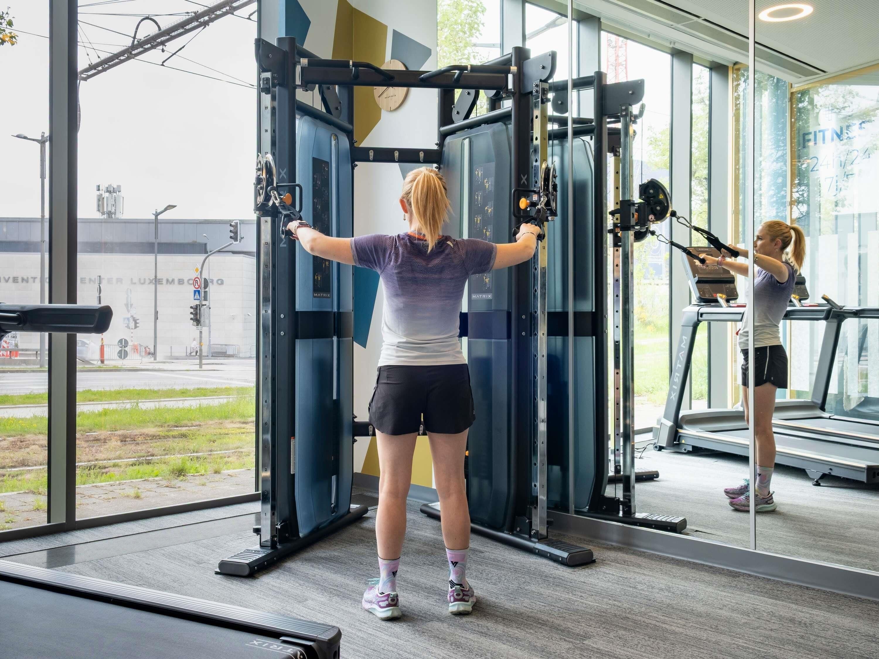 A gym with exercise equipment, a treadmill, and large windows offering a view of the outside.