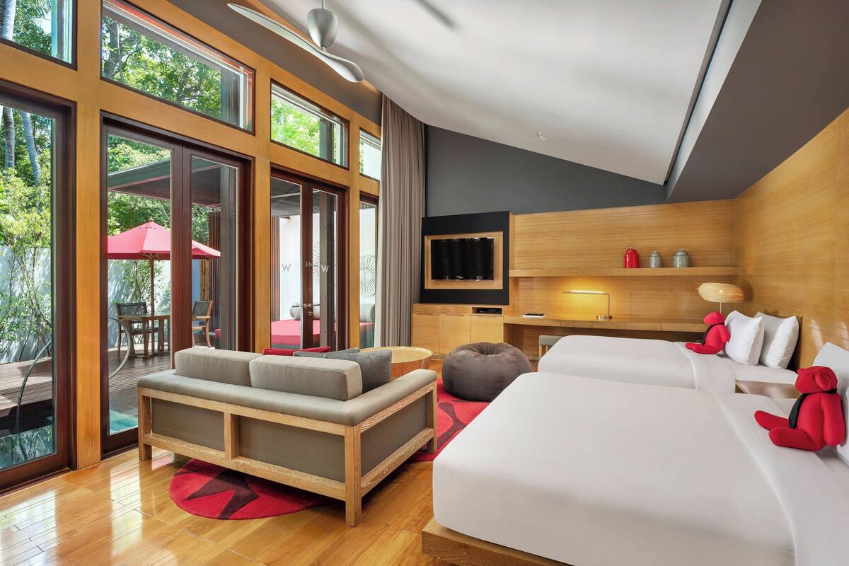 A modern hotel room with a large window, a sofa, a bed, a TV, and a small desk.