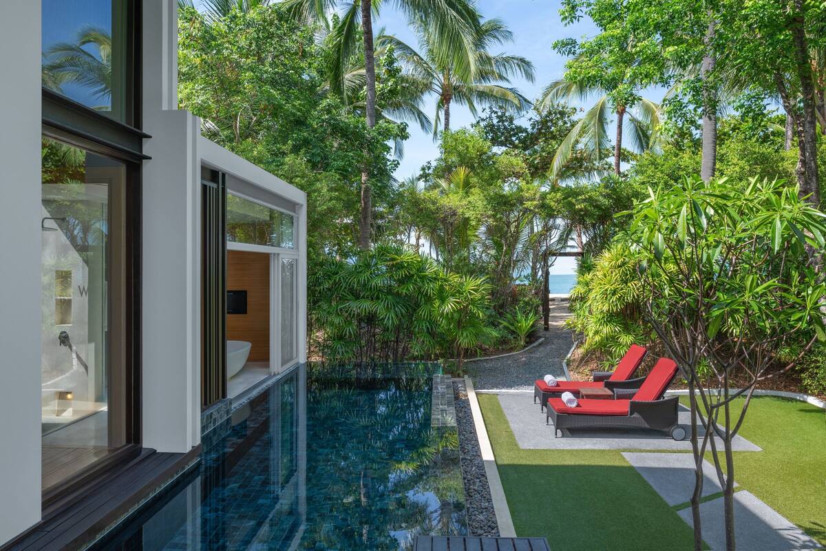 A modern house with a glass-enclosed infinity pool, lush tropical vegetation, and a private outdoor seating area.