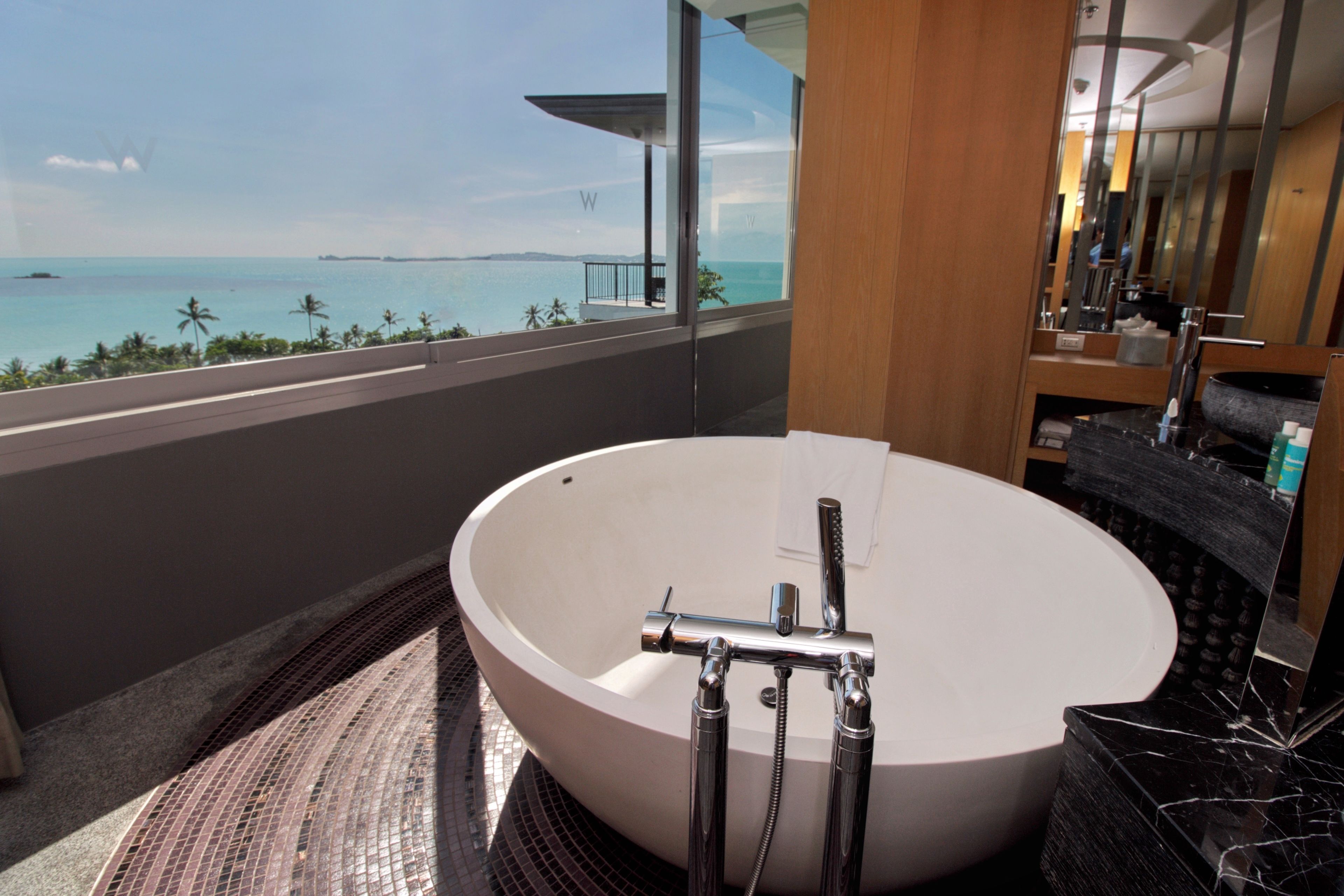 A modern bathroom with a large freestanding bathtub, a vanity with a mirror, and a view of the ocean.