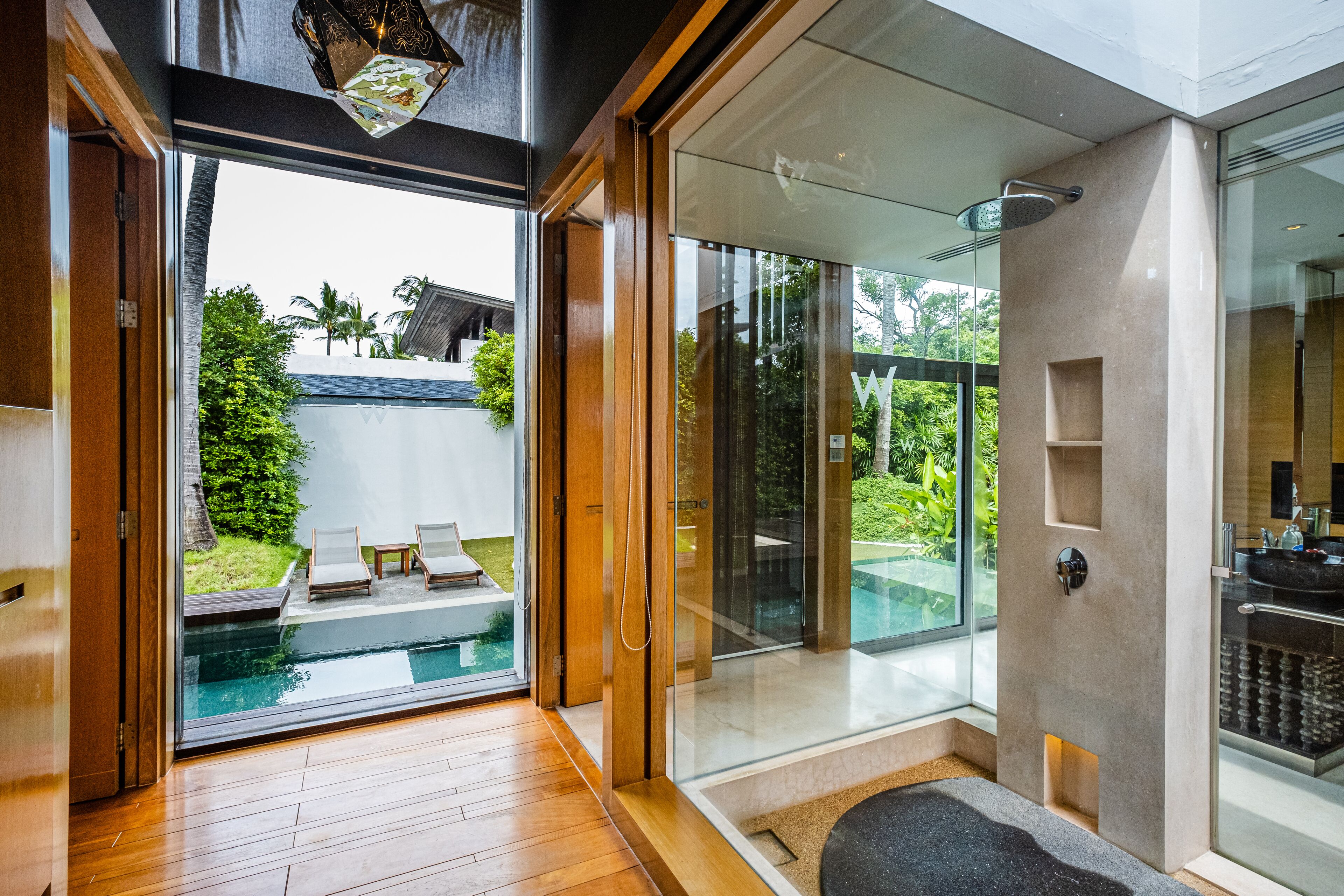 Un baño moderno con cabina de ducha de vidrio, lavabo integrado y vistas a una piscina y zonas verdes al exterior.