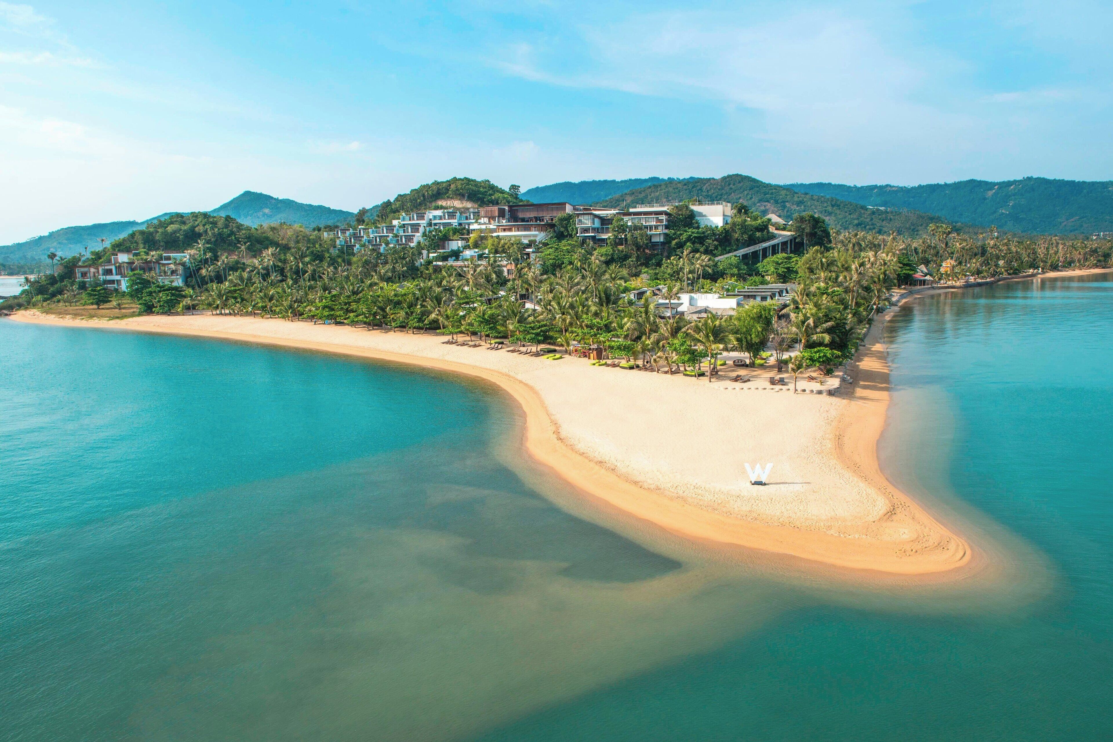 Un complejo turístico frente a la playa con villas, aguas turquesas cristalinas y exuberante vegetación.