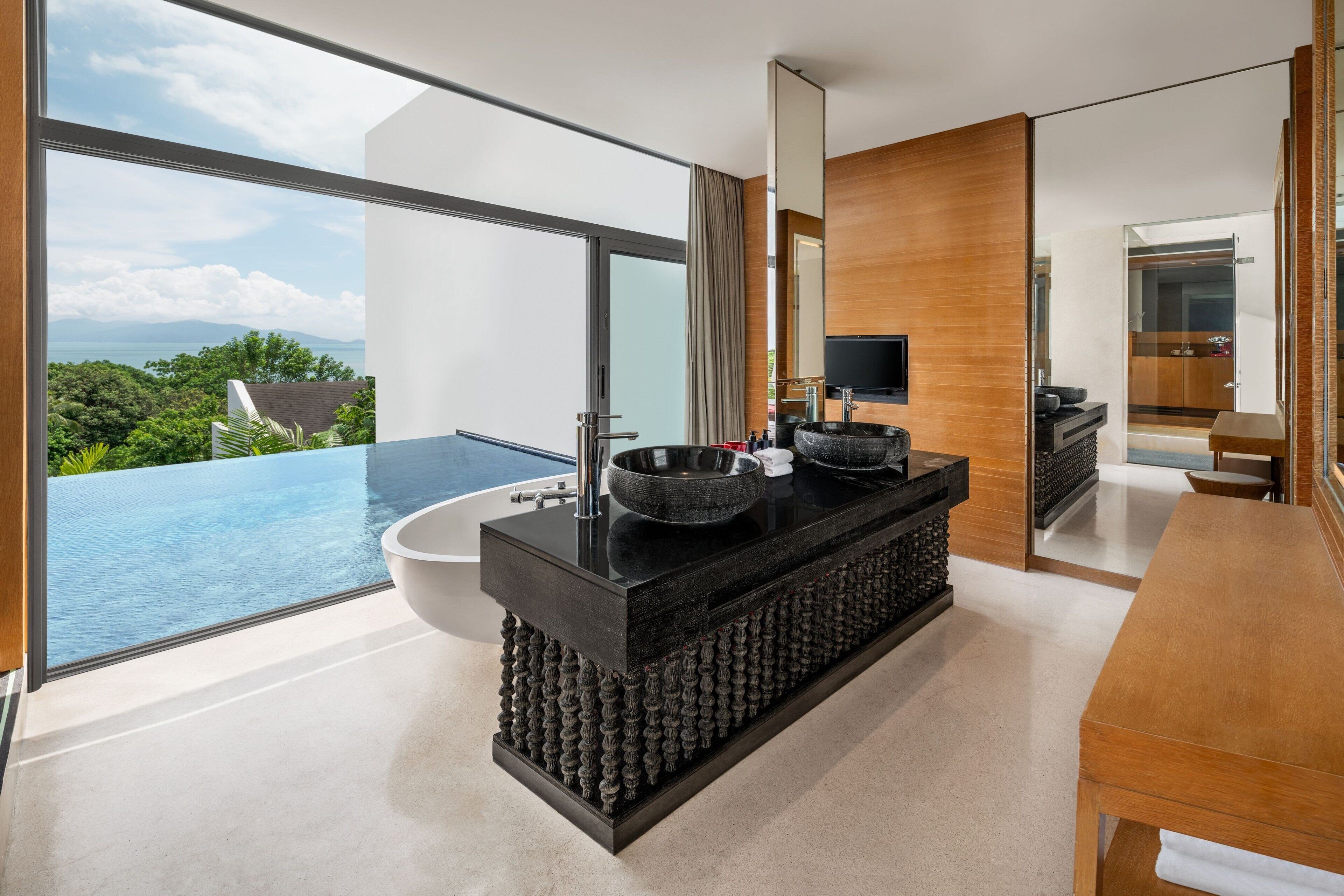 A modern bathroom with a black vanity, a large mirror, and a view of a pool.