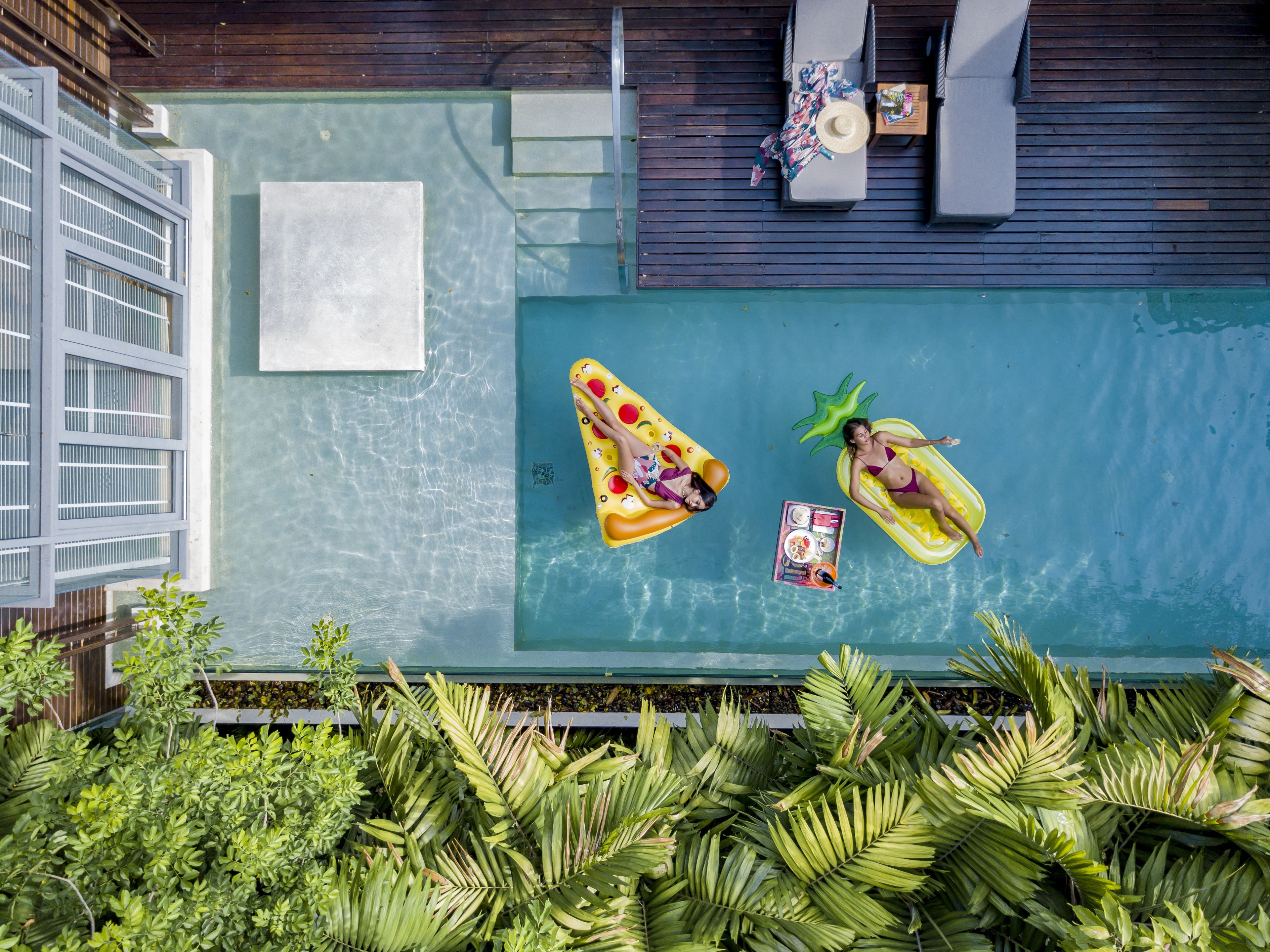 A rooftop pool with two inflatable pools, lounge chairs, and a table with a drink.