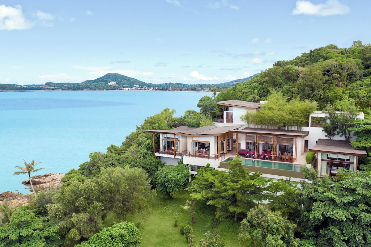 A modern house with a pool, surrounded by lush greenery and overlooking a large body of water.