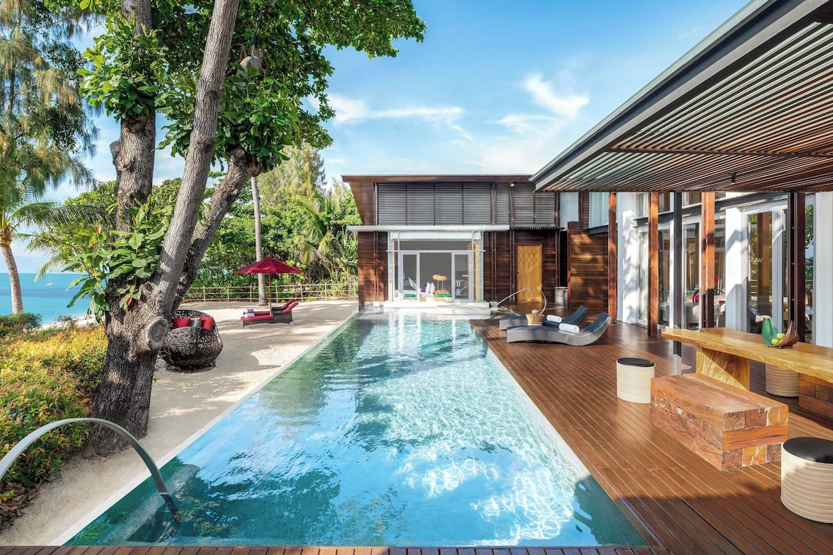 A modern poolside area with a clear view of the sea, wooden deck, and a glass-enclosed pool.