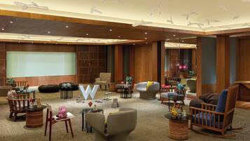A spacious hotel lobby with a large screen, comfortable seating, and a modern ceiling design.