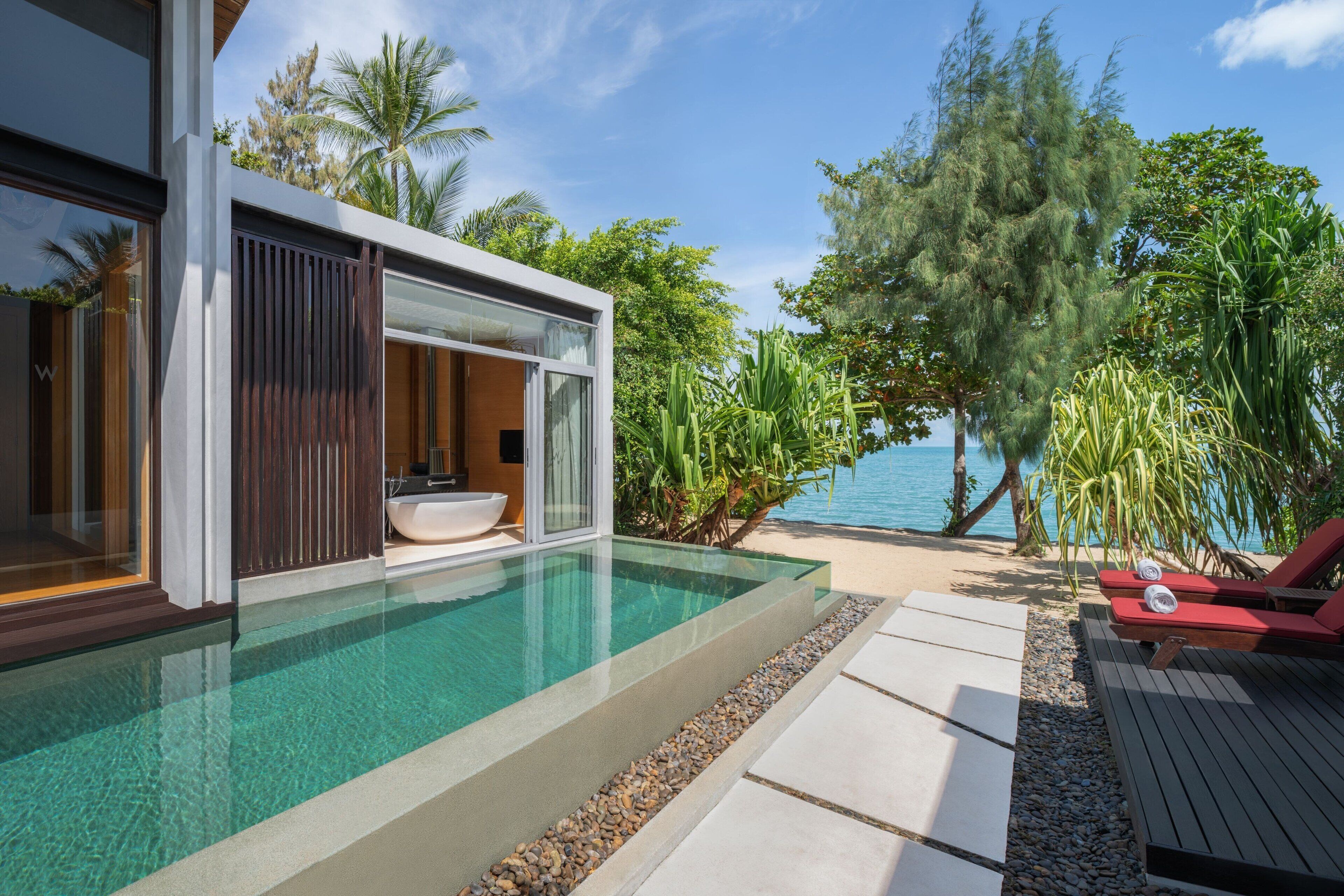 A modern poolside area with a glass-enclosed infinity pool, a wooden deck, and lounge chairs.