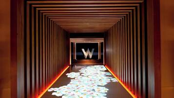 Un pasillo con suelo de madera, un sendero iluminado en el centro y una gran letra 'W' iluminada al final.