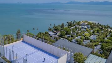 Vista aérea de una zona residencial con cancha de tenis, casas y una playa al fondo.
