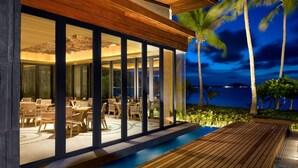 A modern outdoor dining area with wooden tables and chairs, large glass doors, and a wooden deck overlooking a body of water. - W Koh Samui (Koh Samui)