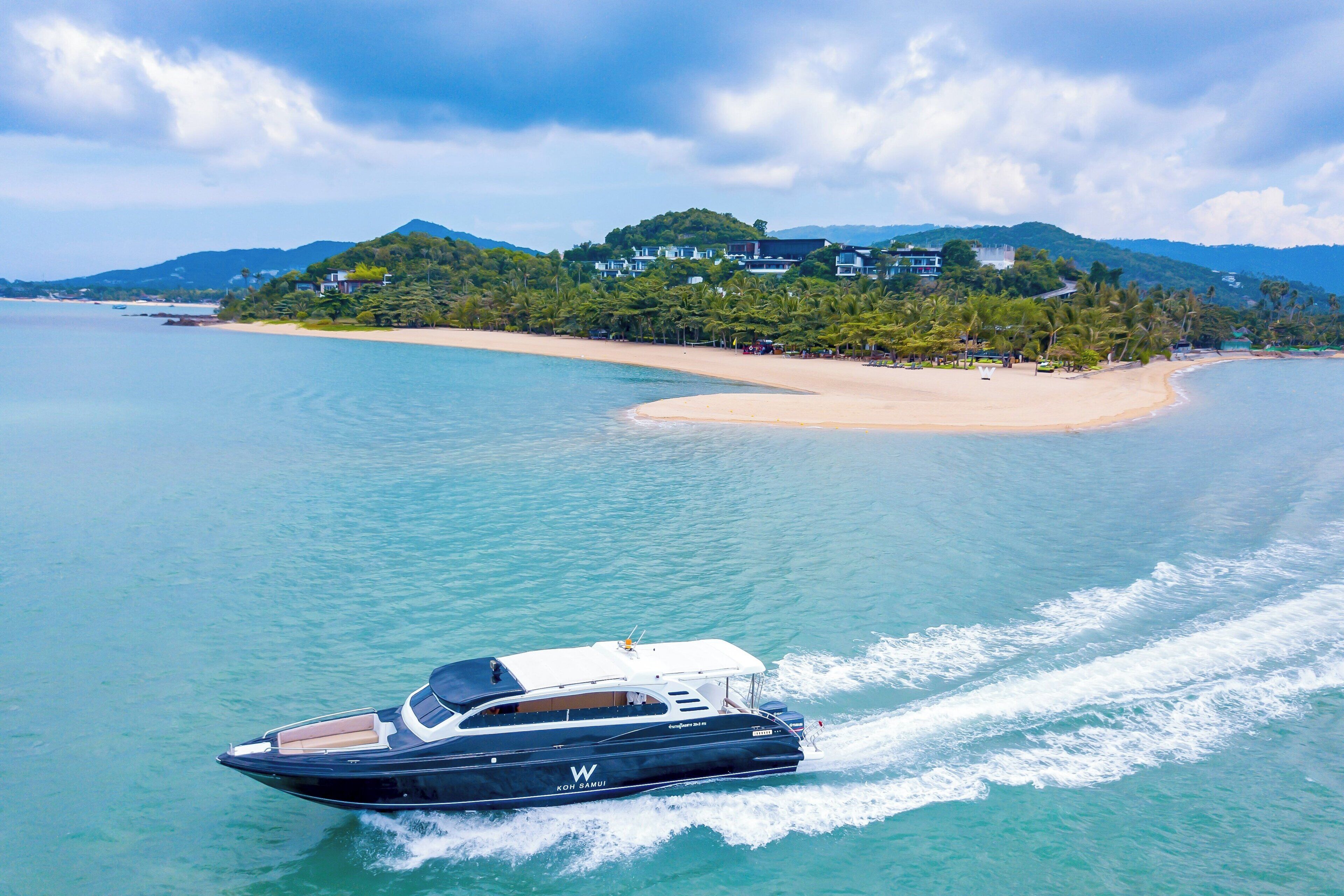 A yacht on a calm sea with a beach and buildings in the background.