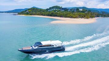 A yacht on a calm sea with a beach and buildings in the background.