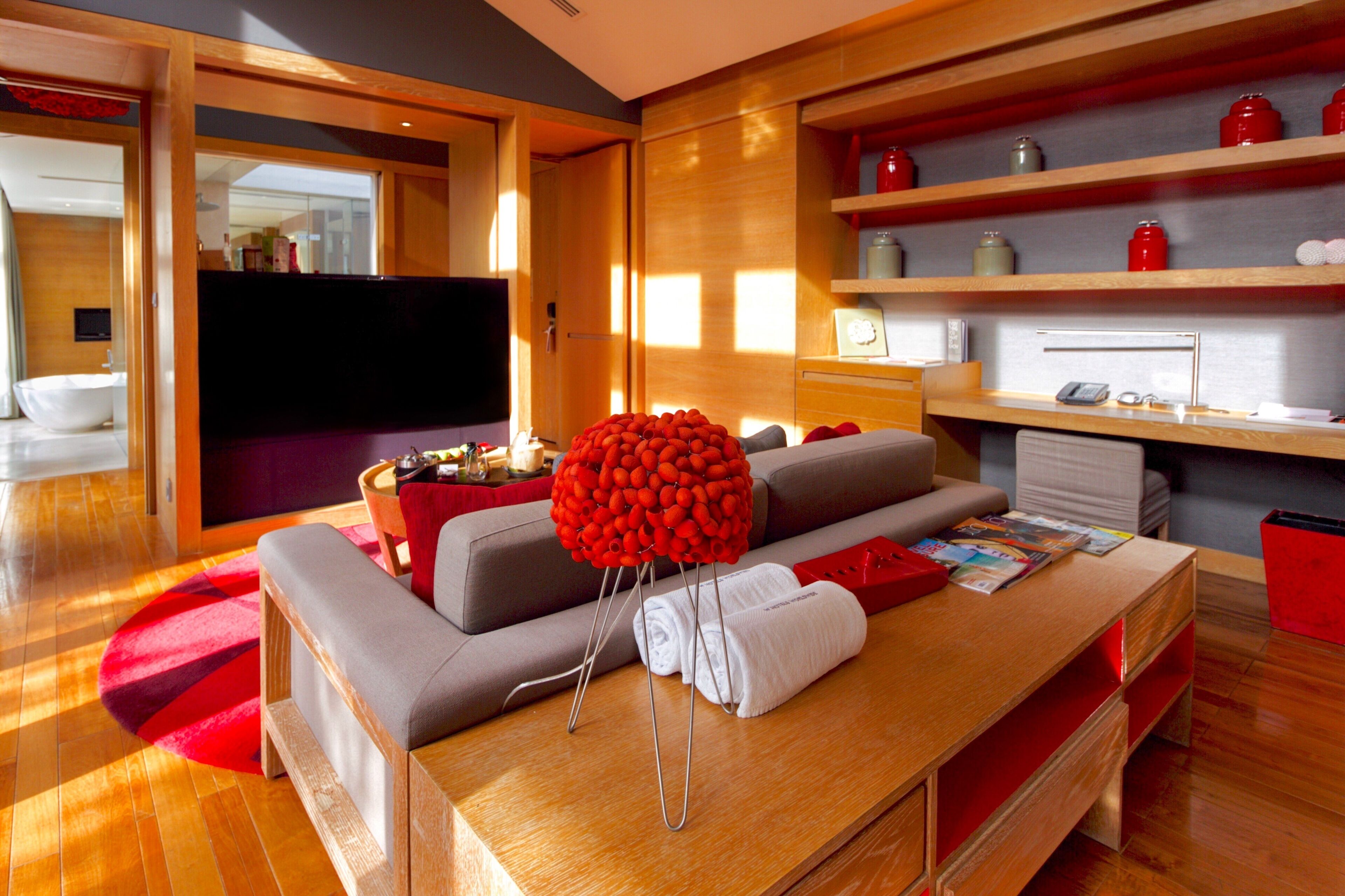 A modern living room with a wooden coffee table, grey sofa, and red accents.
