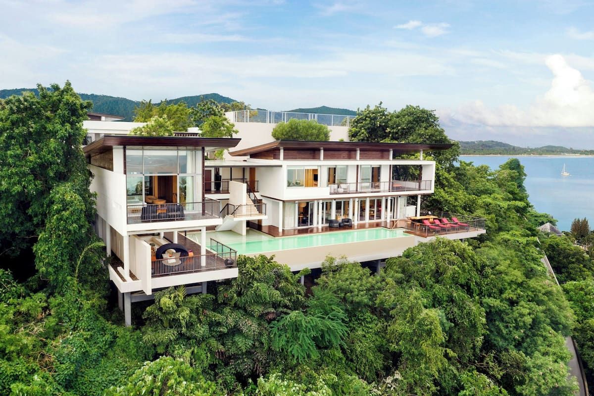 A modern two-story house with a large glass balcony, a swimming pool, and a view of the sea.