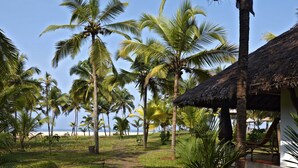 A pathway leading to a thatched-roof structure surrounded by palm trees and a beach in the background. - Neeleshwar Hermitage (Hosdurg)
